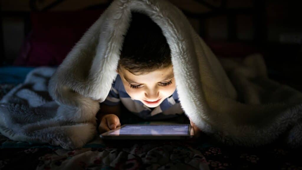 Quanto tempo de tela é demais para seus filhos? Curadoria 45 Heroes: Menino jogando jogos de tablet na cama